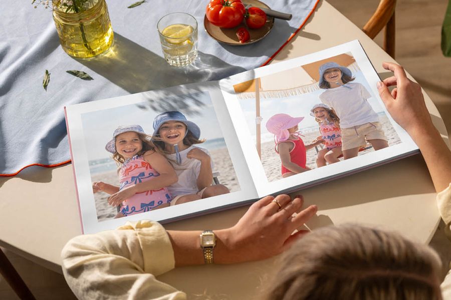 Een geopend fotoboek op een keukentafel toont foto's van jonge meisjes die plezier hebben op het strand, ter illustratie van albelli's tip om terug te blikken op zomerherinneringen met een persoonlijk fotoboek.