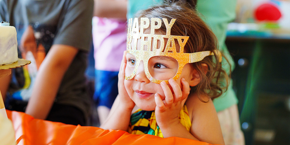 Een jong meisje met een vrolijke Happy Birthday feestbril, op zoek naar een verjaardagscadeau of origineel verjaardagscadeau van albelli.