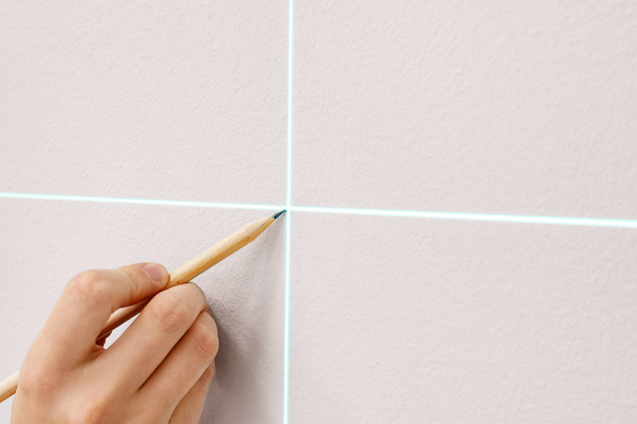 Een hand markeert een muur ter voorbereiding op het ophangen van wanddecoratie, ter illustratie van albelli's stap-voor-stap tip om de muur te markeren voordat je een frame-hangkit installeert.