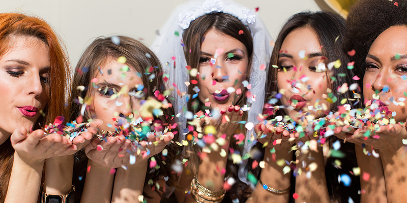 Een vrouw met een sluier die confetti blaast met vier vriendinnen, ter inspiratie voor een vrijgezellenfeest bij albelli.