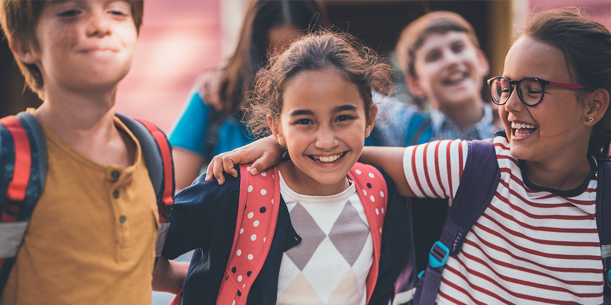 Drie schoolvriendjes omhelzen elkaar en glimlachen naar de camera, als beeld van de vreugde van de eerste schooldag in albelli's gids voor prachtige schoolfoto's.