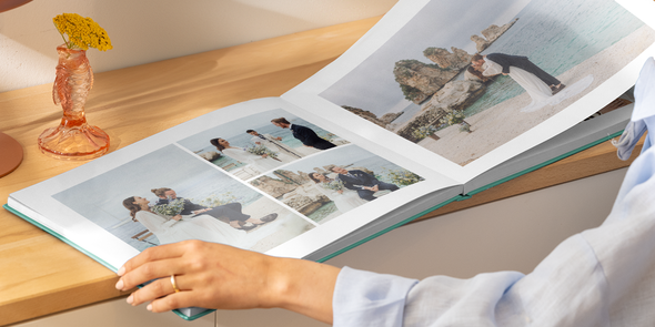 Handen van een vrouw die een opengeslagen trouwfotoboek vasthouden, met een dubbele pagina vol verschillende strandfoto’s van een bruid en bruidegom, ter illustratie van albelli’s ideeën voor de titel van je trouwfotoboek.