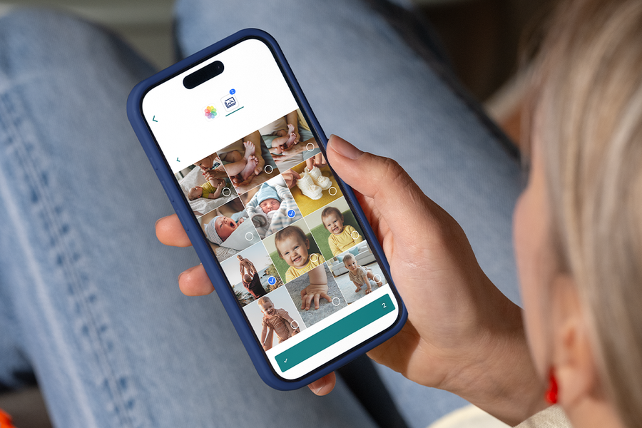 Een hand die babyfoto's selecteert op een smartphone om een gepersonaliseerd eerste jaar fotoalbum te maken bij albelli.