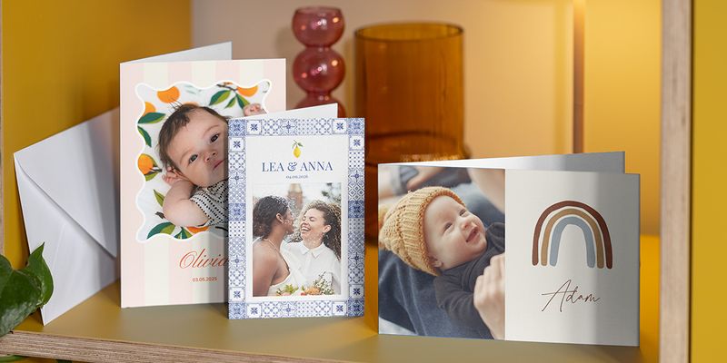 Een selectie van fotokaarten op een plank, waaronder geboortekaartjes en een trouwkaart; ideaal om te zien hoe je zelf een fotokaart maken kunt bij albelli.