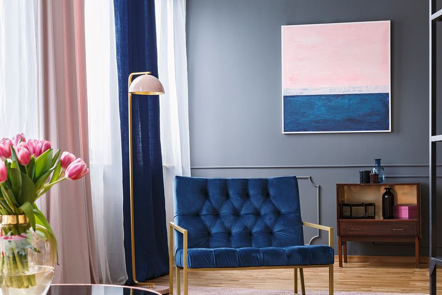 Een marineblauw met roze woonkamer met een blauwe fluwelen bank, kleurrijke gordijnen en roze tulpen, als voorbeeld van een huurvriendelijke woonkamer bij albelli.