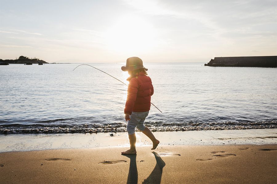 Een kind staat op het strand bij de zee met een sterke schaduw achter zich, als illustratie van het dramatische effect van silhouetfotografie in zonlicht.