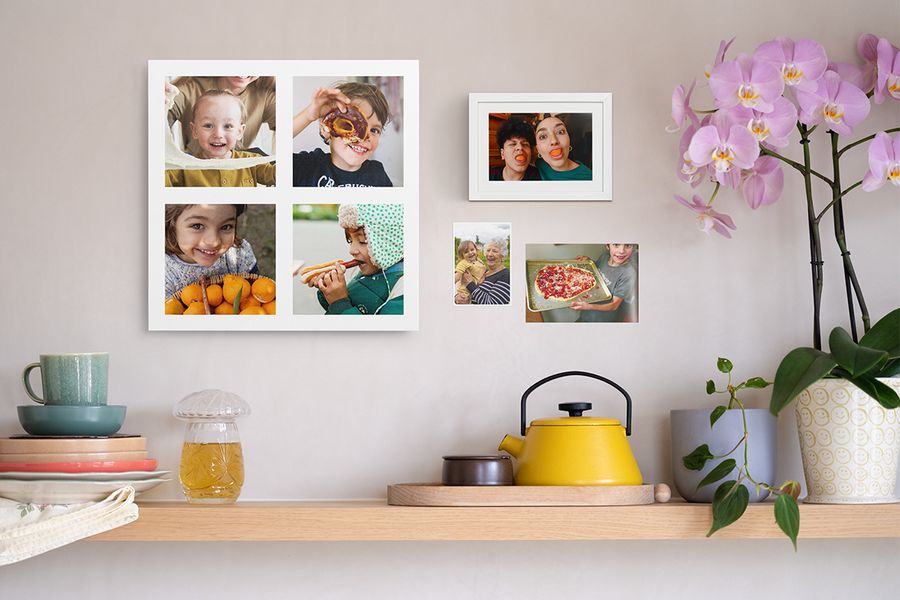 Een houten plank met gezellige woonaccessoires staat onder een gepersonaliseerde fotocollage van kinderen, een grappige ingelijste fotoafdruk en twee fotoafdrukken van het gezin, als inspiratie om foto’s aan de muur te brengen.