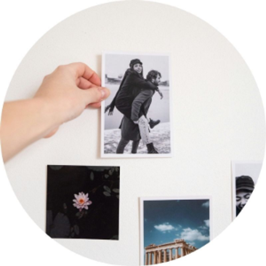 Een hand houdt een fotoafdruk van een stel vast naast andere fotoafdrukken, als illustratie van Andrea’s aanzoekverhaal en een betekenisvol aanzoekidee vol herinneringen van albelli.
