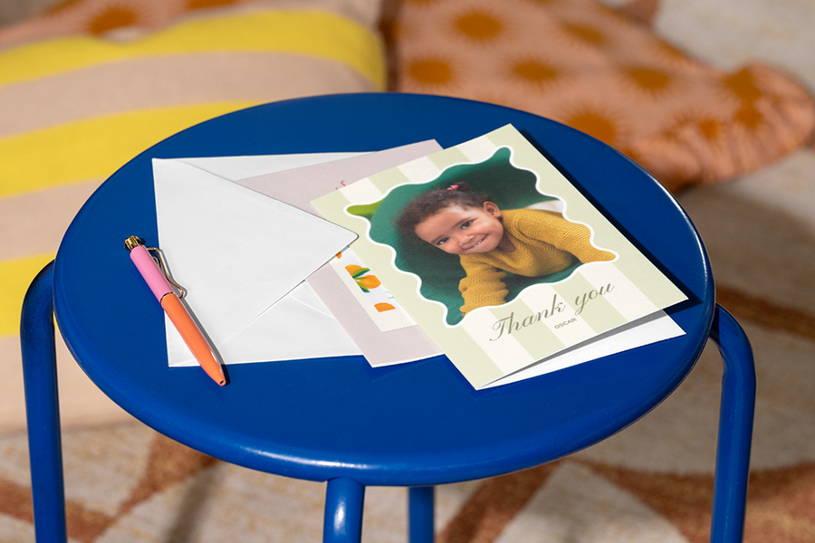 Een gepersonaliseerde albelli kaart voor docent met een foto van een klein meisje op de voorkant ligt op een krukje met een pen ernaast, als inspiratie voor een bedankje voor docent met een warme en respectvolle boodschap.