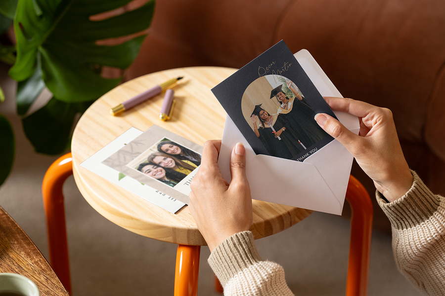 Handen stoppen een gepersonaliseerde albelli bedankkaart voor een leerkracht met afgestudeerden op de voorkant in een envelop.