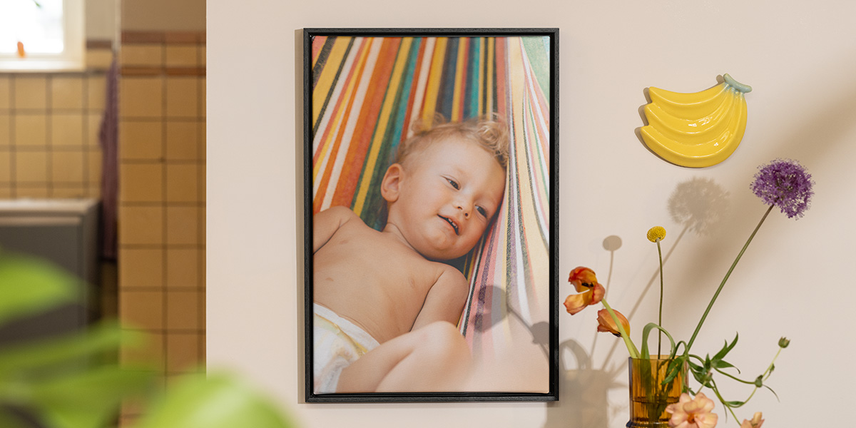 Gepersonaliseerde albelli wanddecoratie met een babyfoto naast bloemen en fruitdecoratie, als inspiratie voor vrolijke zomer decoratie in huis.
