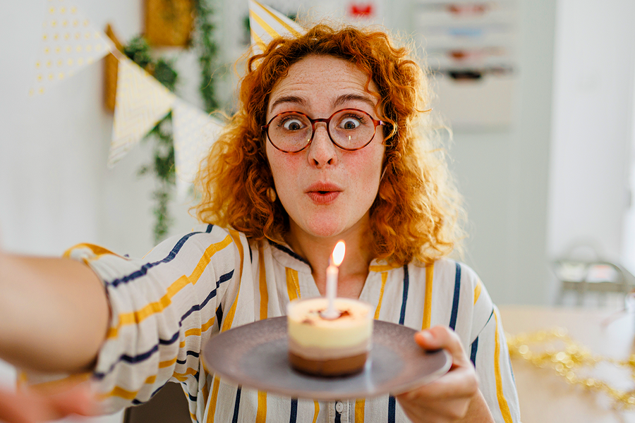 Een vrouw met rood krullend haar houdt een cupcake met een kaars vast, als inspiratie voor verjaardagswensen voor een collega en verjaardagskaart ideeën van albelli.