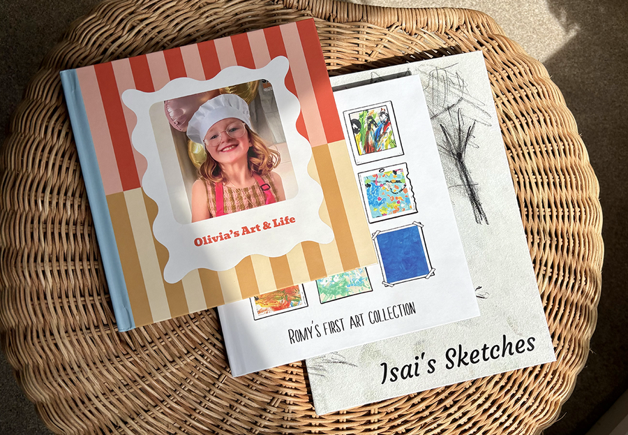 Drie kinderfotoboeken liggen op elkaar gestapeld op een salontafel, elk met kunstwerken van een andere leeftijdsgroep, van schilderijen van jonge kinderen tot tekeningen van tieners, ter illustratie van de voordelen van een albelli kinderfotoboek.