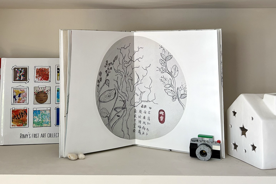Een geopend kinderfotoboek toont een volledige paginaspreiding van boomschetsen met tekst, naast een gesloten fotoboek met een omslag in scrapbookstijl met verschillende voorbeelden van kindertekeningen, ter illustratie van het betekenisvolle aandenken dat een albelli kinderfotoboek creëert.
