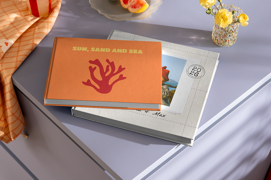 Twee fotoboeken liggen op elkaar gestapeld, waarbij het bovenste boek een koraalmotief en de titel 'Sun, Sand and Sea' heeft, ter illustratie van albelli's fotoalbum titel ideeën voor een strandvakantie.