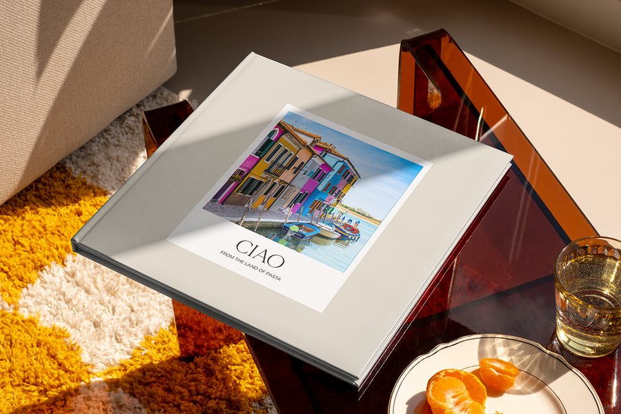 Een fotoboek met een kanaal en kleurrijke huizen in Italië op de cover heet 'Ciao from the Land of Pasta', ter illustratie van albelli's fotoalbum titel ideeën voor stedentrips.