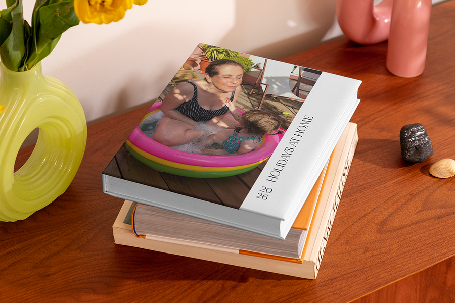 Een stapel fotoboeken heeft boven op een boek met een vrouw en een jong kind in een opblaaszwembadje, met de titel 'Holidays at Home', ter illustratie van albelli's fotoalbum titel ideeën voor een vakantie thuis.