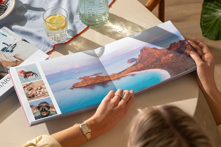 Een geopend reisfotoboek op een tafel toont een dubbele pagina met een prachtig strandlandschap, aangevuld met drie zomerse foto's, ter illustratie van albelli's Travel Chapter-ontwerp uit de nieuwe Summer Travel Series.