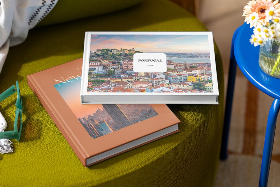 Twee gepersonaliseerde fotoboeken staan op elkaar gestapeld op een krukje, het bovenste met de titel 'Portugal' en een foto van Portugal, en daaronder een boek met de titel 'New York' en een foto van de stad, ter illustratie van albelli's personaliseerbare Summer Travel Series ontwerpen.