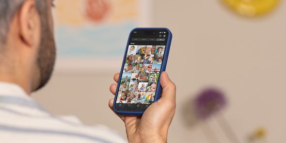 Een man houdt zijn telefoon omhoog en scrolt door zijn camerarol, ter illustratie van albelli's gids om foto-overload aan te pakken en foto's op te ruimen.