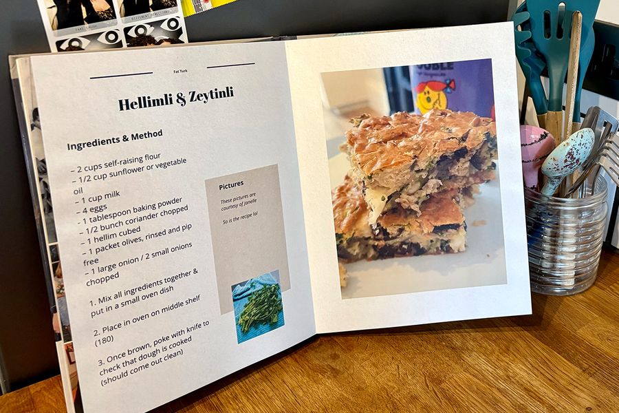 Een geopend gepersonaliseerd kookboek staat in een keuken, met een pot met lepels en keukengerei op de achtergrond, ter illustratie van albelli's tips om te bepalen welke recepten je opneemt voordat je je eigen kookboek maakt.