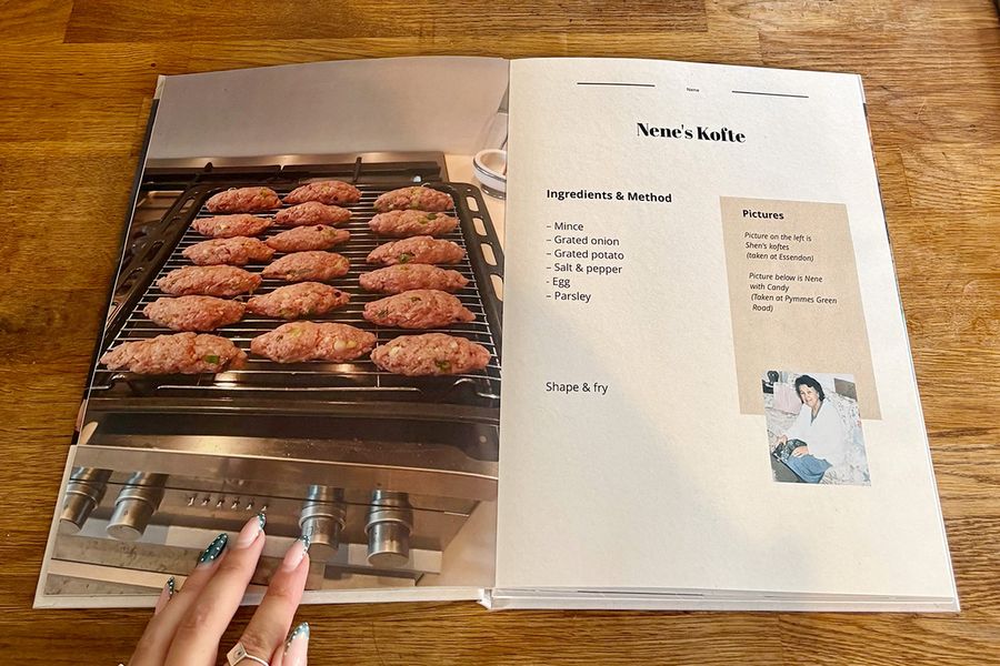 Een geopende spread uit Sarah's kookboek toont het kofte-recept van haar Nene, met de gemanicuurde hand van een vrouw rustend op het boek op een houten aanrecht, ter illustratie van albelli's laatste checklist-tips voordat je een gepersonaliseerd kookboek laat afdrukken.