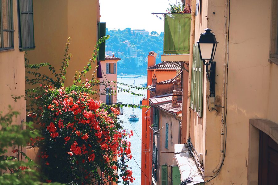 Een smalle straat vol bloemen leidt naar de zee in Nice, als beeld van de charme van een septembervakantie in de Zuid-Franse kust.