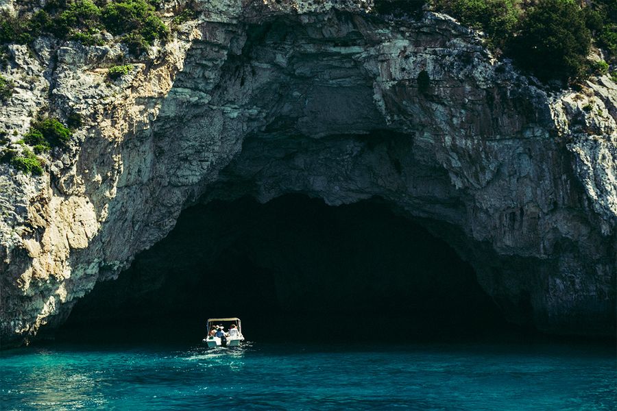 Een boot vaart een zeegrot binnen op Corfu, als beeld van het rustige tempo en de schoonheid van een Griekse eilandvakantie in september.