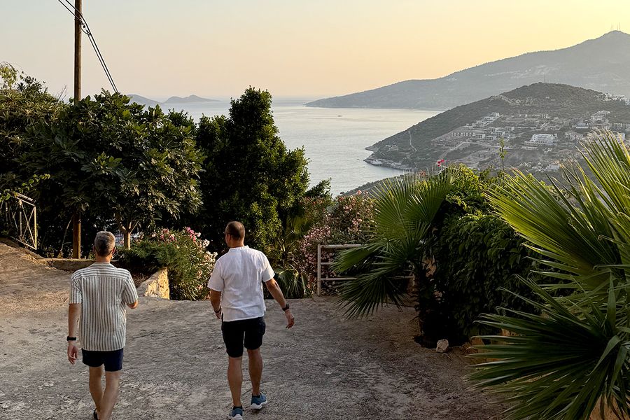 Twee mannen lopen een heuvel af, omringd door planten, richting de zee in Kalkan, als beeld van de charme van een Turkse septembervakantie aan de Turkoois Kust.