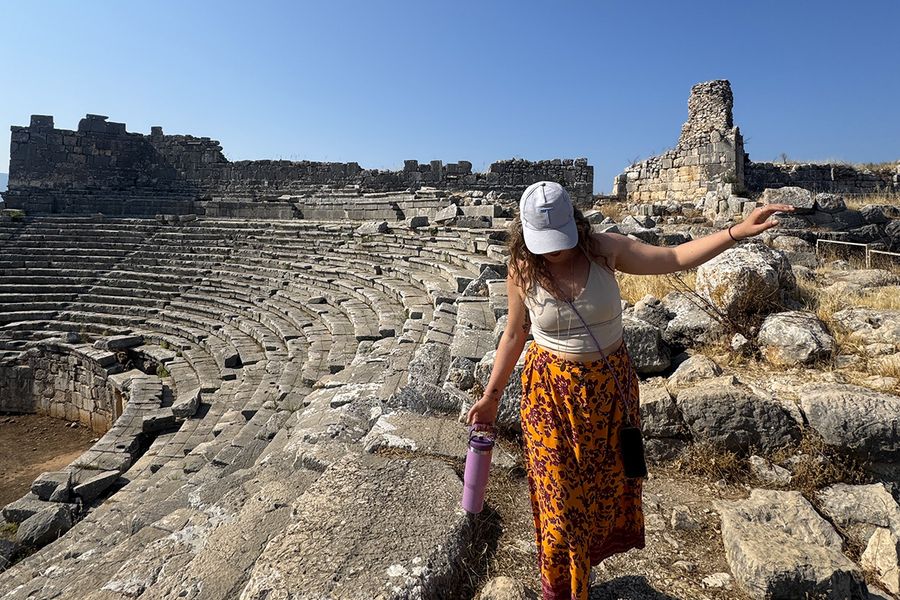 Gemma, copywriter bij albelli, loopt tussen de rotsen van een amfitheater in Kalkan, Turkije, ter illustratie van hoe je de juiste septemberbestemming voor je vakantie kiest.