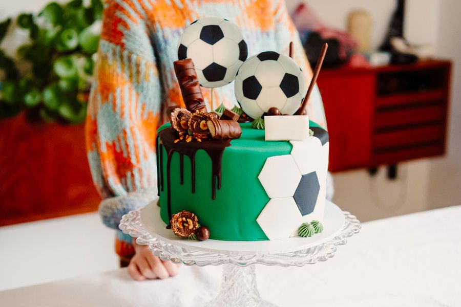 Een verjaardagstaart voor een kind, versierd met voetballen en chocoladerepen, ter illustratie van albelli's tip om de showstopper-taart te fotograferen voordat de gasten arriveren.