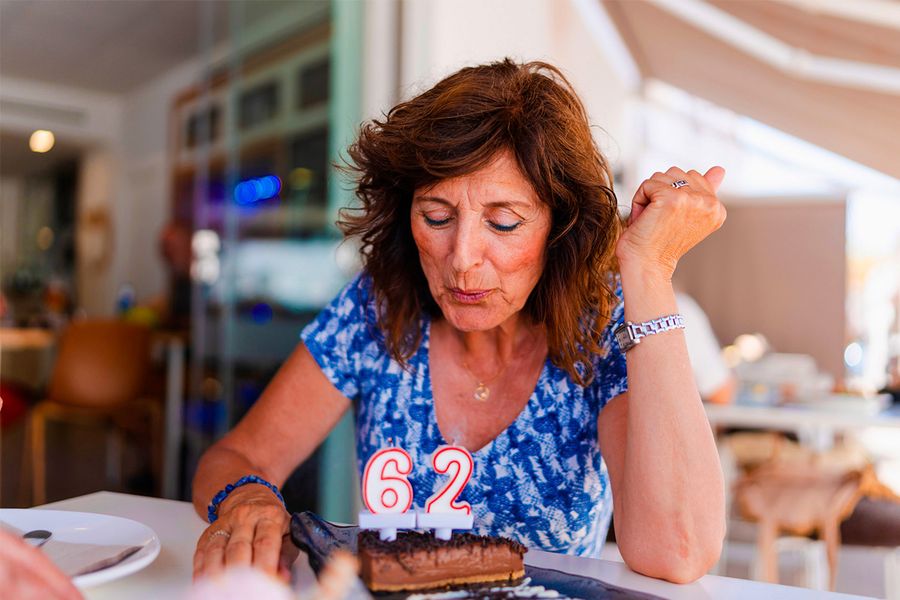 Een vrouw blaast de kaarsjes uit met het cijfer '62' op haar verjaardagstaart, ter illustratie van albelli's tip om het exacte moment vast te leggen waarop de kaarsjes worden uitgeblazen.