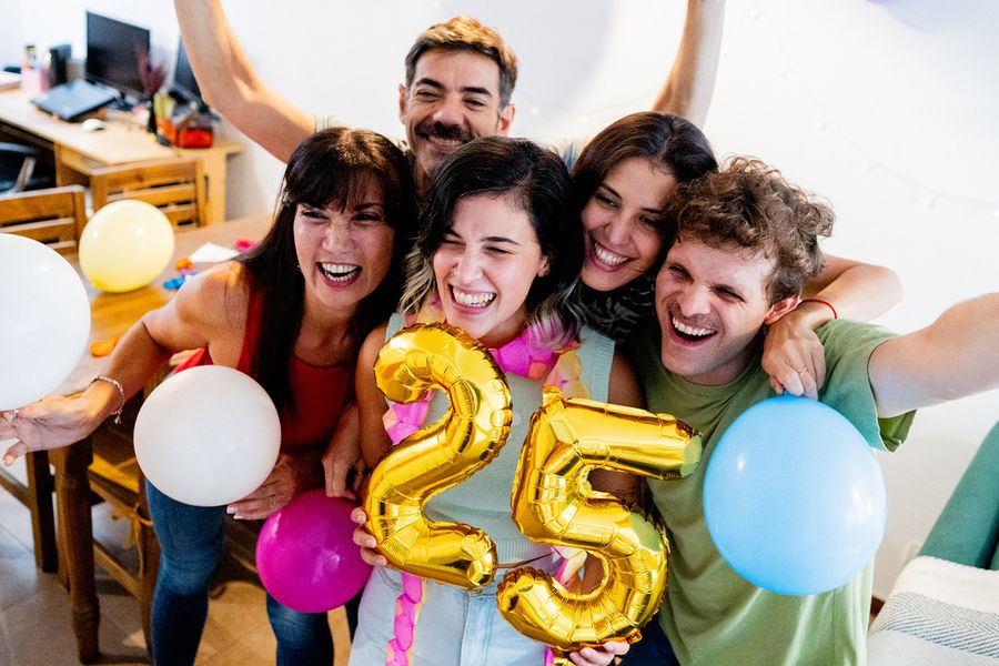 Een groep jonge mensen verzamelt zich rond ballonnen met het cijfer '25', lachend en poserend voor een foto, ter illustratie van albelli's tips om mijlpaal-verjaardagsmomenten vast te leggen.