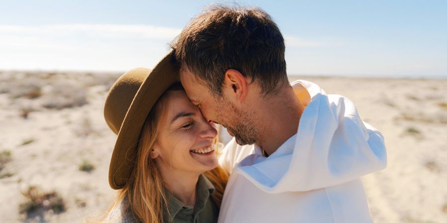 Een koppel van in de dertig lacht en omhelst elkaar in een strandachtige, woestijnachtige omgeving, ter introductie van albelli's gids met 60 ideeën voor huwelijksjubileumkaarten.