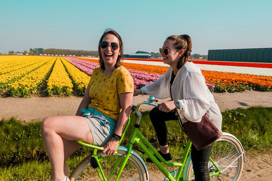Twee vrouwen fietsen samen, lachend en giechelend in een bloemenveld, ter illustratie van albelli's ideeën voor wat je kunt schrijven in een huwelijksjubileumkaart voor vrienden.