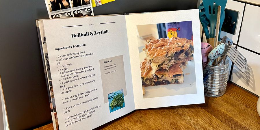 Een geopend gepersonaliseerd kookboek staat in een keuken, met een pot met lepels en keukengerei op de achtergrond, ter introductie van albelli's gids om je eigen kookboek te maken.