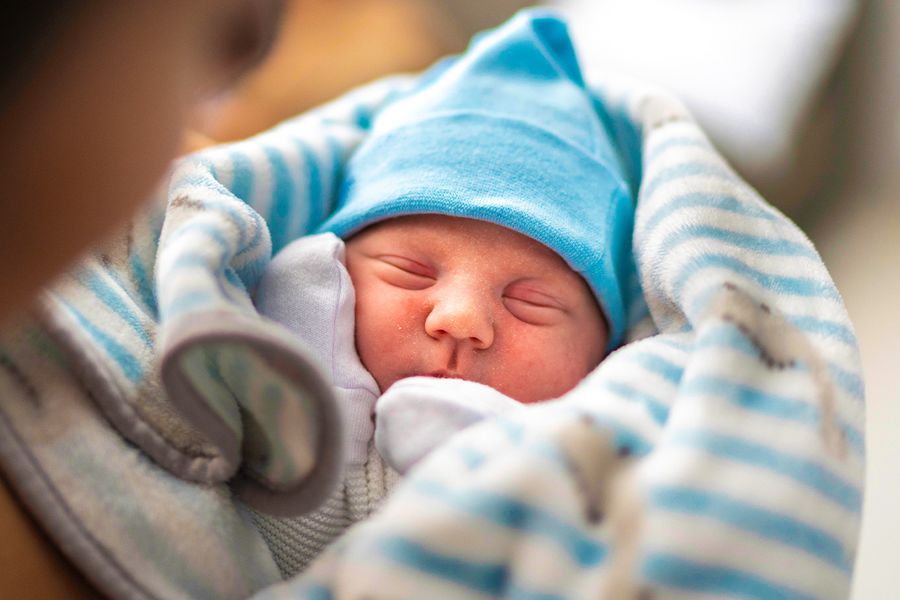 Pasgeboren baby ingebakerd in een blauw-wit gestreepte deken met een blauwe muts op, ter illustratie van albelli’s ideeën om de eerste kerst van een baby te vieren met iets persoonlijks.