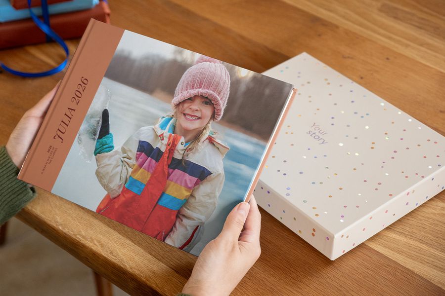 Iemand houdt een fotoboek met de titel 'Julia' vast, met een lachend meisje op de cover, met een presentatiecadeaudoos net achter op de tafel, ter illustratie van waarom een fotoboekdoos een creatie extra speciaal maakt.