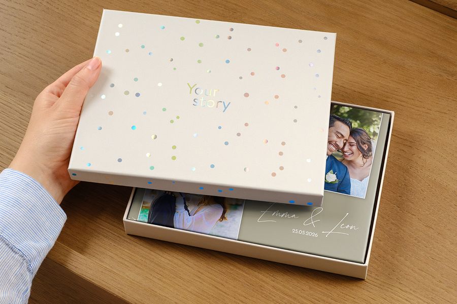 Een trouwfotoboek staat in de nieuwe presentatiedoos, met op de cover een foto van het koppel en de trouwdatum als titel, deels verborgen door het op een kier staande deksel van de cadeaudoos, ter illustratie van waarom een presentatiedoos de moeite waard is voor een premium trouwfotoboek.
