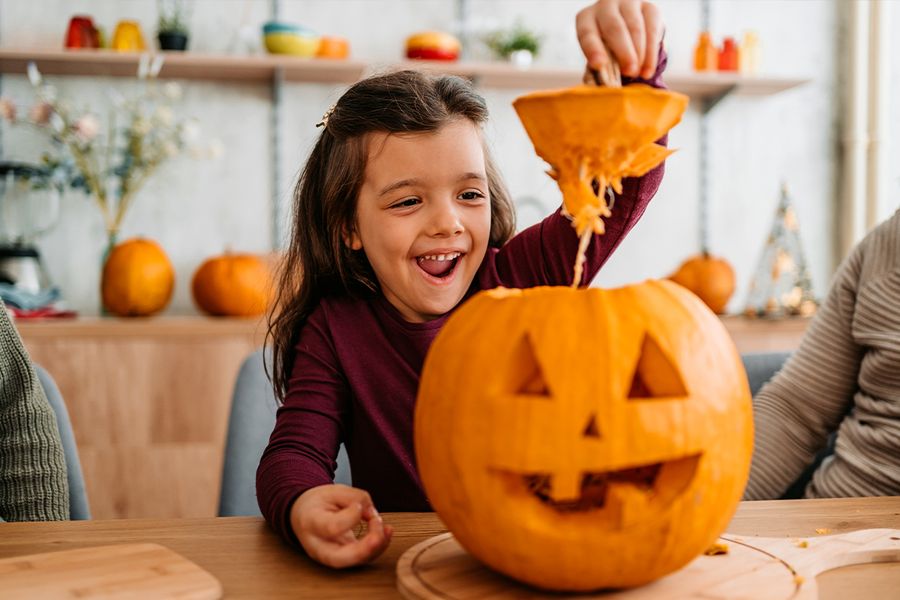Een kind trekt de bovenkant van een pompoen af die het net heeft uitgesneden, ter illustratie van albelli's grappige en schattige pompoenteksten voor Halloween-bijschriften op Instagram.