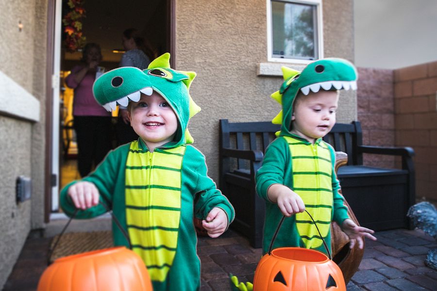 Twee kleine jongens in dinosauruspakken gaan trick or treaten met pompoenmandjes in hun handen, ter illustratie van albelli's Halloween-teksten voor foto's van snoep ophalen.
