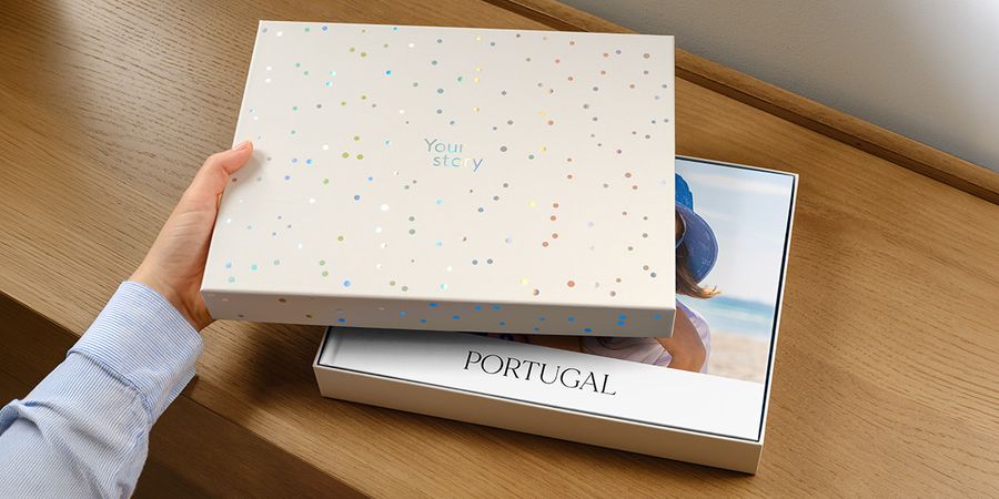 Een albelli presentatiedoos staat met het deksel op een kier, waardoor een gepersonaliseerd reisfotoboek voor Portugal zichtbaar wordt, met de cover deels verborgen door het deksel, ter introductie van albelli's nieuwe fotoboek-cadeaudoos.