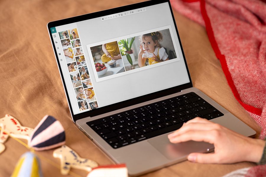 Een hand op het touchpad van een laptop ontwerpt een fotoboek op het scherm, met een dubbele pagina van een meisje en een kom aardbeien, ter illustratie van albelli’s online editor voor Black Friday-kerstcadeaus.
