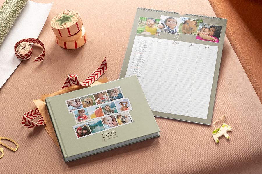 Een saliegroen fotoboek met 2026 op de omslag en een familiewandkalender met foto's bovenaan en kolommen voor elk gezinslid, ter illustratie van albelli’s gedeelde familiekalender voor Black Friday-kerstcadeaus.