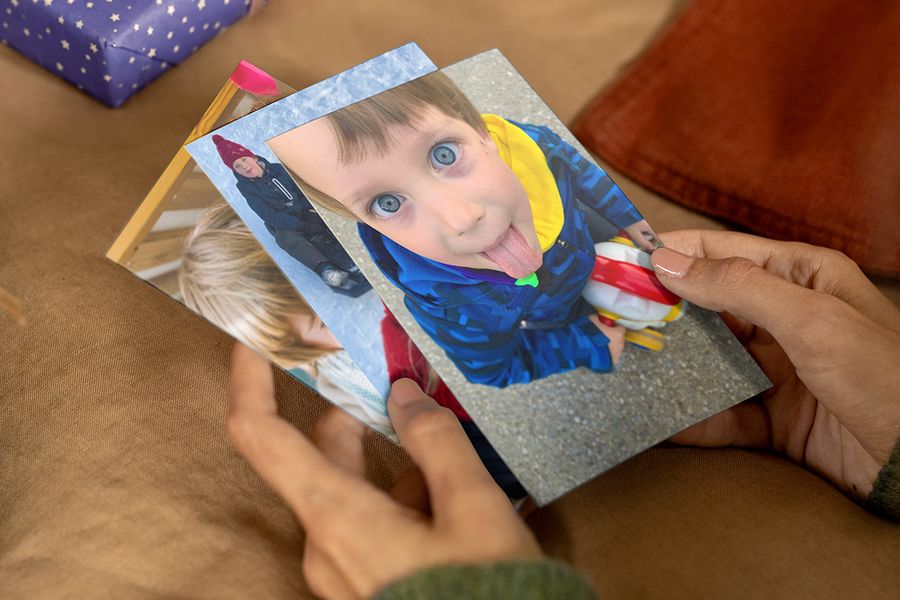 Twee handen die gedrukte foto’s uitwaaieren, met op de voorste foto een kind in een blauw jasje met de tong uit de mond, ter illustratie van albelli’s tip om grappige prints toe te voegen aan de Sinterklaasverrassing.
