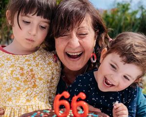 Een oma viert haar 66e verjaardag met haar twee kleinkinderen naast zich en staat op het punt de kaarsjes op haar taart uit te blazen, als inspiratie voor verjaardagscadeaus uit de ultieme verjaardagscadeaugids van albelli.