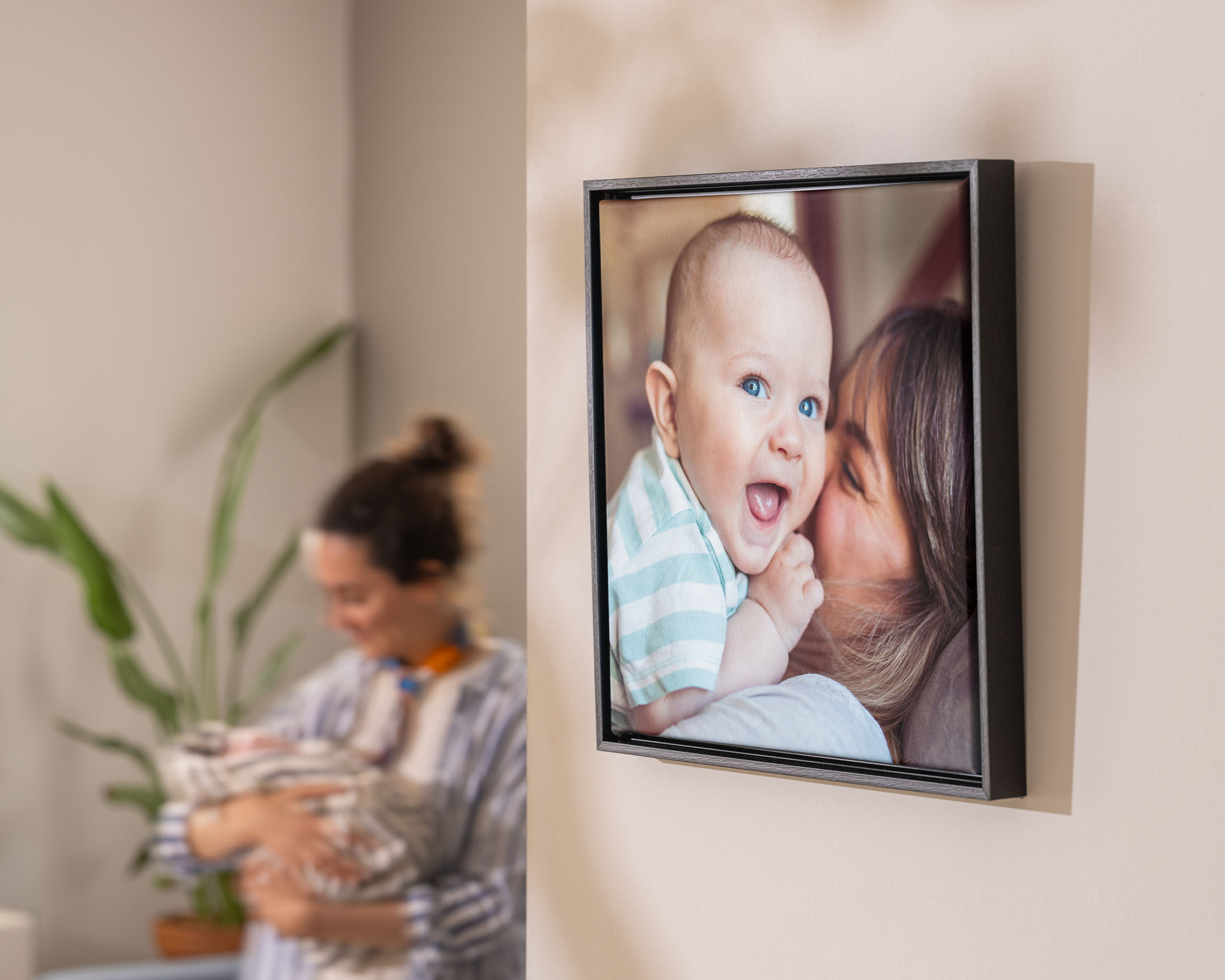 Een muur met een ingelijste foto op canvas van een moeder die haar baby knuffelt.