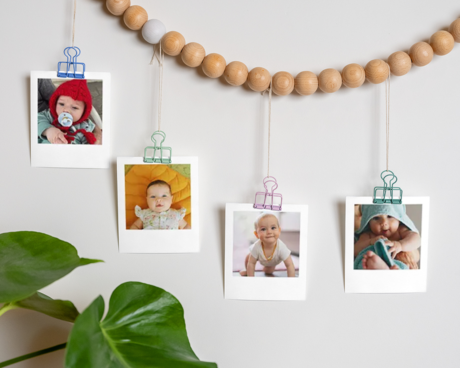Babyfoto's aan een houten kralenslinger aan de muur.