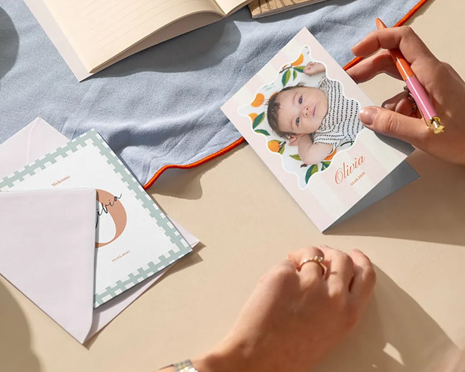 Handen schrijven een gepersonaliseerde babyfotokaart op een bureau.