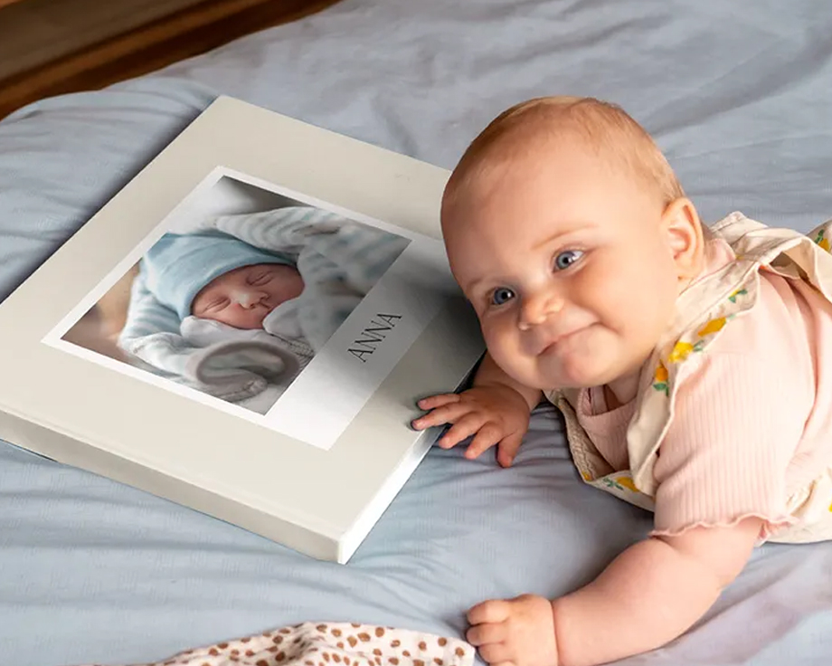 Een baby ligt naast een gepersonaliseerd fotoboek met een babyfoto op de kaft.